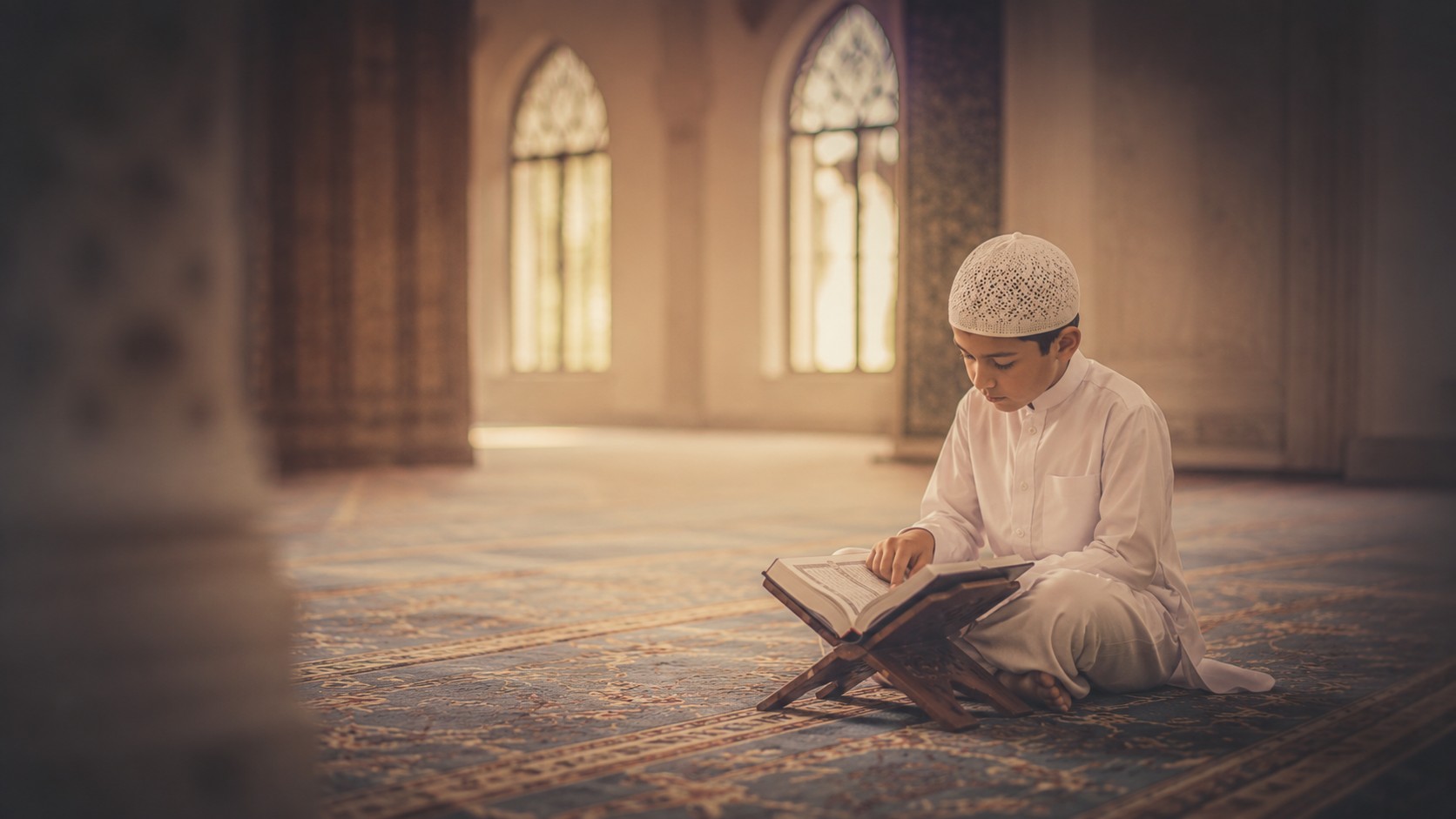 A young student reading the Quran from a wooden rehal